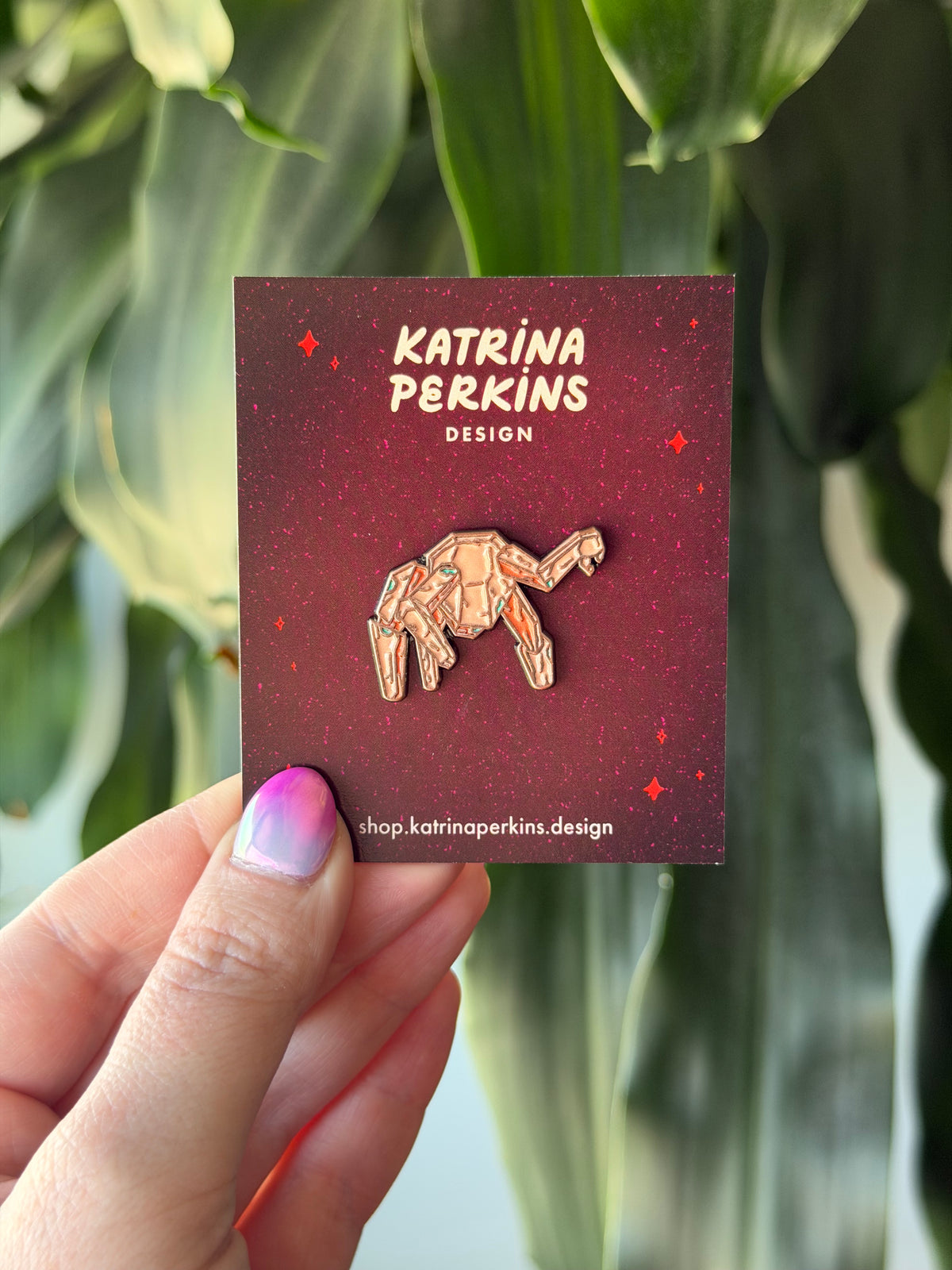 Rocky pin on a red card with 'Katrina Perkins Design' branding, held against a green leafy background.