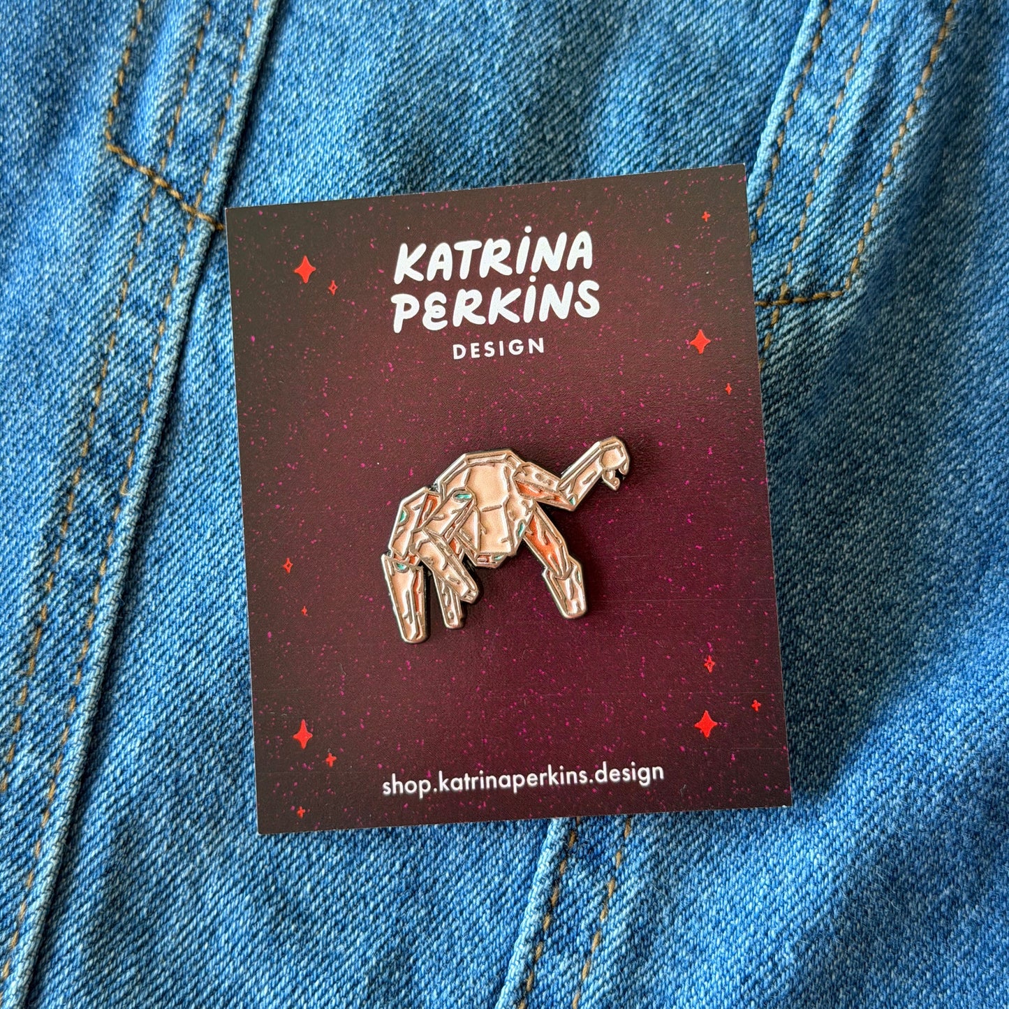 Pin on a card with 'Katrina Perkins Design' branding, placed on blue denim fabric.